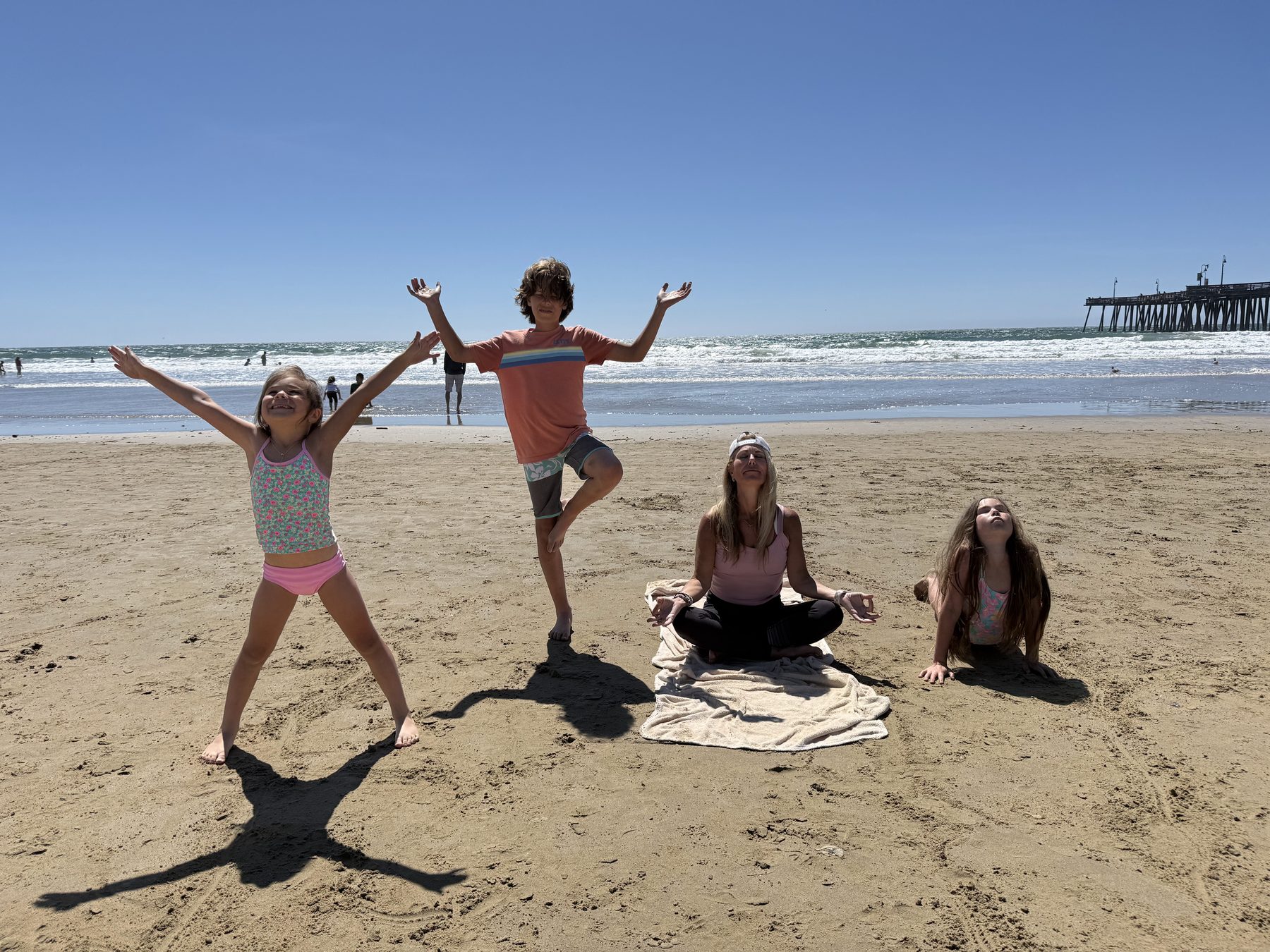 Dana meditating while kids do their own yoga poses around her on the beach