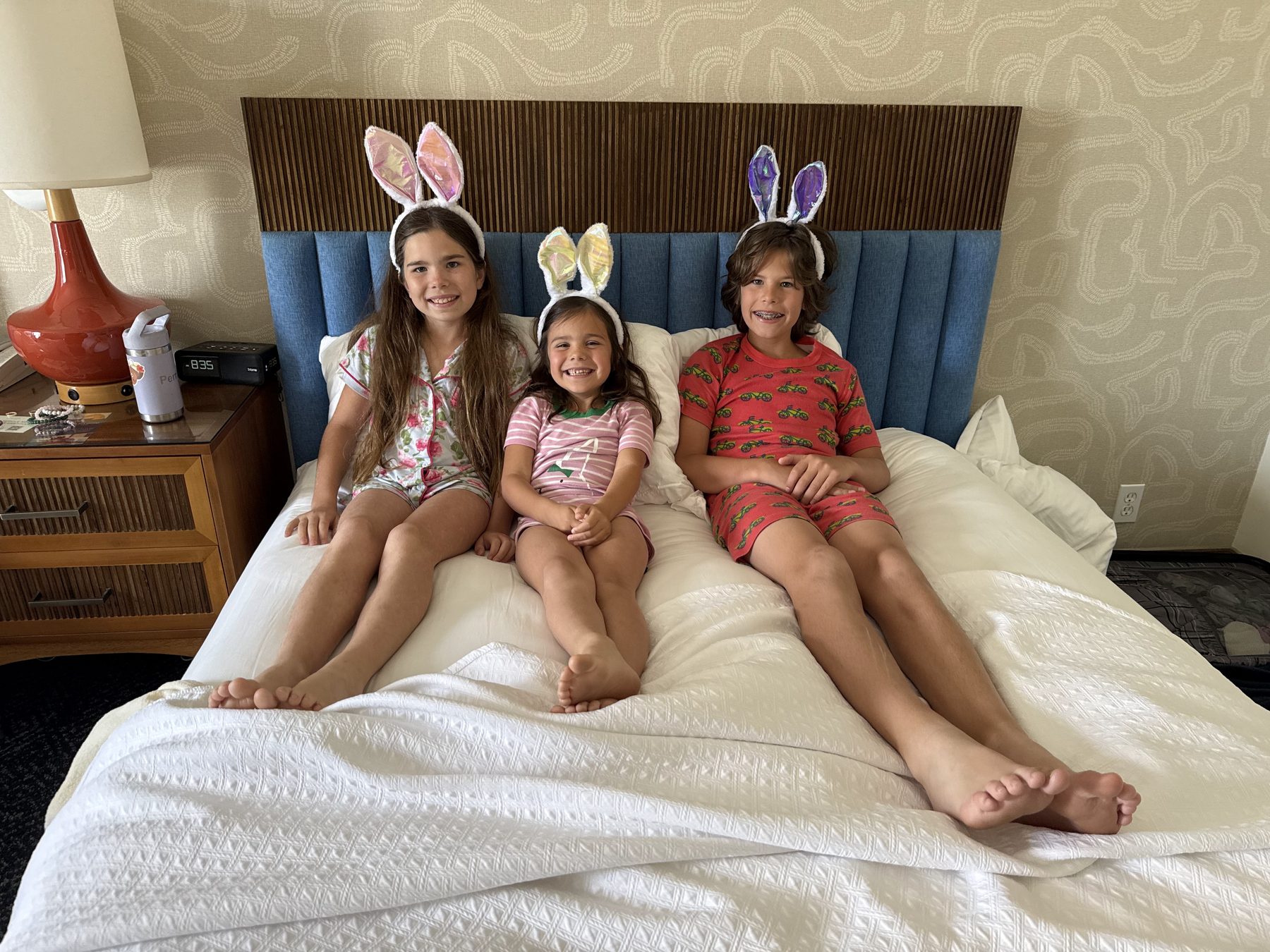 Three kids in pajamas and bunny ears sitting on the hotel bed