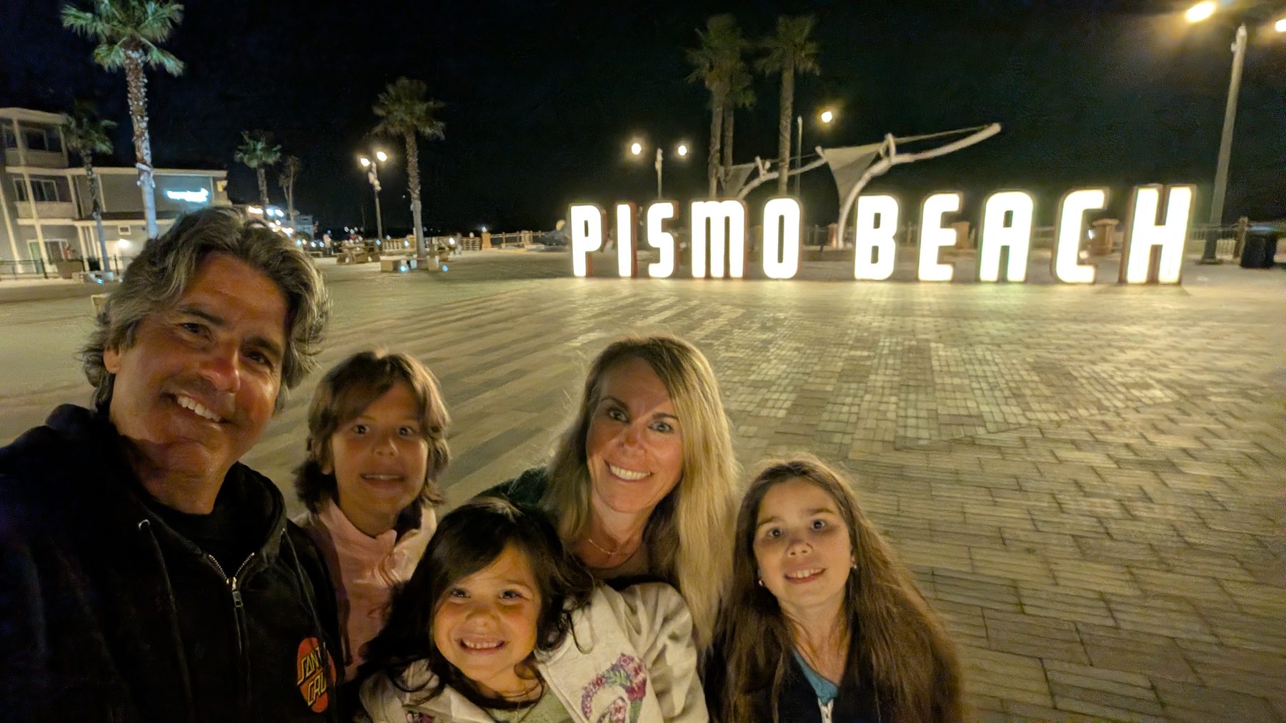 Leone family selfie in front of the lit Pismo Beach sign at night