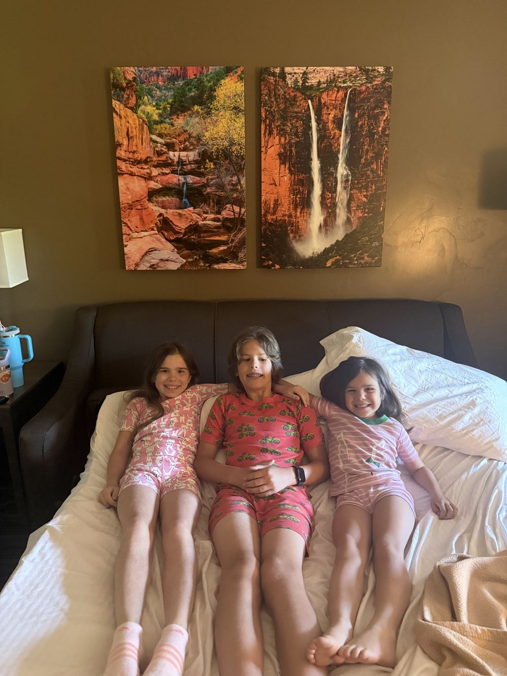 Three kids in pajamas on hotel bed — Zion art on wall